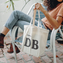 Load image into Gallery viewer, DoubleBlind: Woman sitting in chair holding the DoubleBlind Tote Bag.
